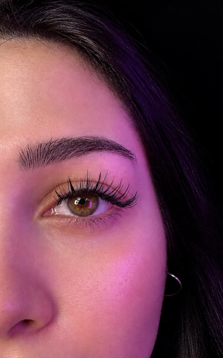 Detalle de un ojo con extensiones de pestañas, de cerca y con luz rosa