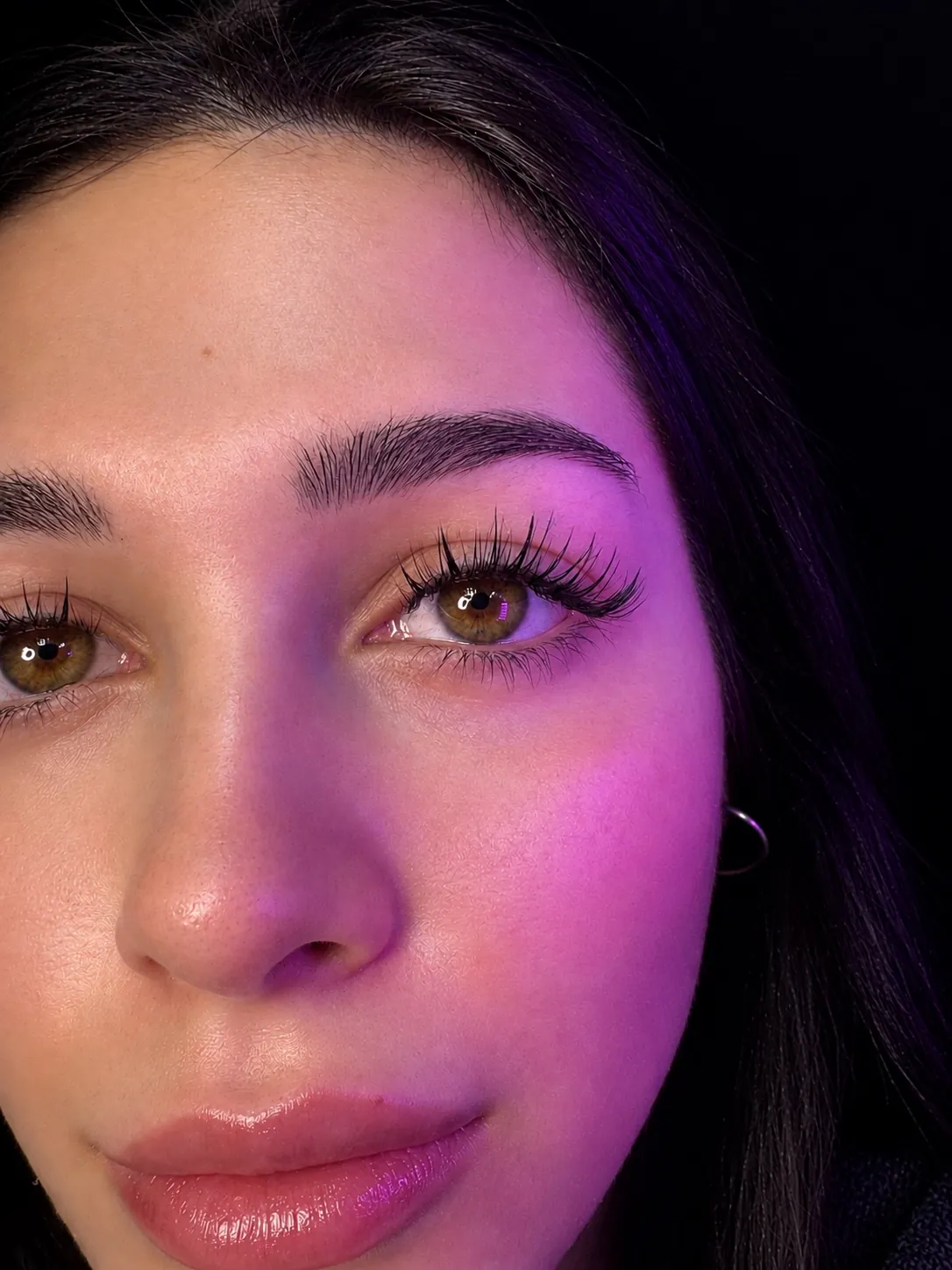 Rostro con extensiones de pestañas, iluminado con luz rosa